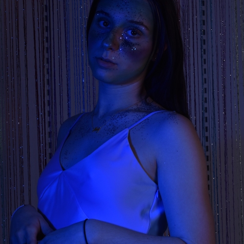 Person in white dress and glitter all over posing for the camera with a blue glow