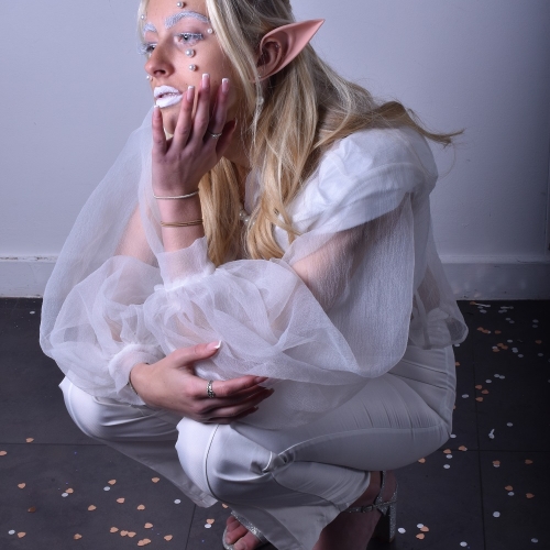 Person crouched posing in white attire with elf ears