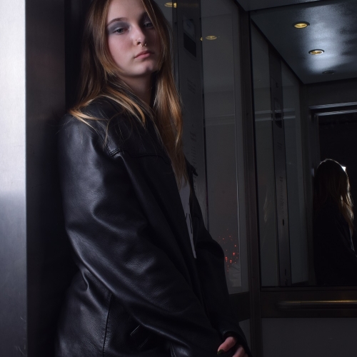 person posing inside an elevator with a black leather jacket