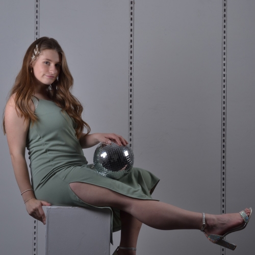person sitting on a block in a greenish dress, one leg stretched out and holding a disco ball
