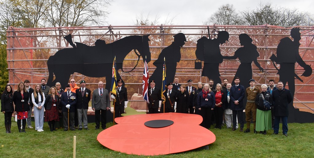 Group photo in front of wooden mural tribute to the fallen for Remembrance 2022 at West Suffolk College