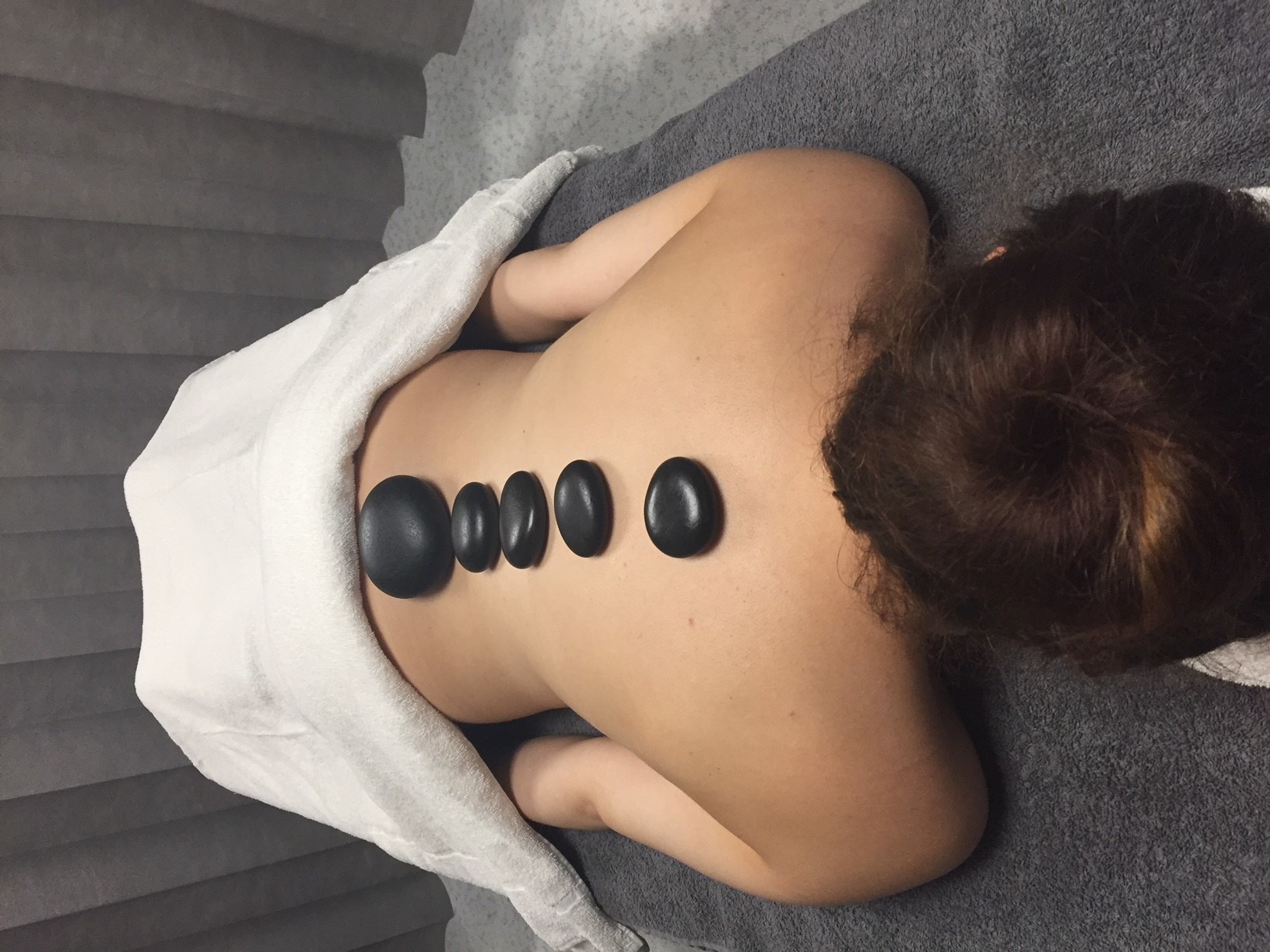 Photo of a woman face down on a table with hot stones laid on her spine