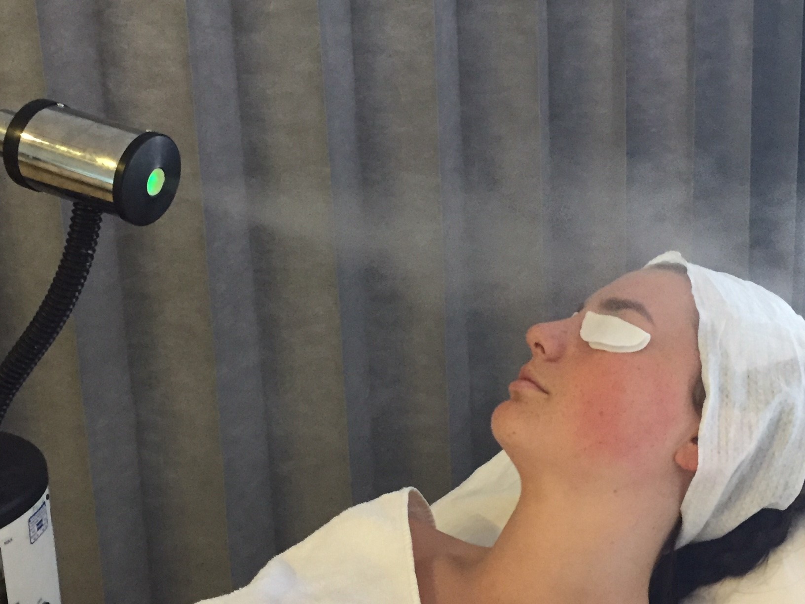 Photo of a woman laying down with a machine spraying a fine mist at her face