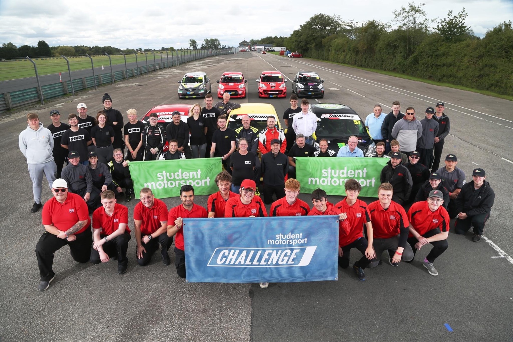Motorsport students posing with banners by racing cars