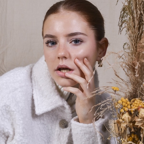 closeup of a person with a white fluffy jacket posing next to flowers