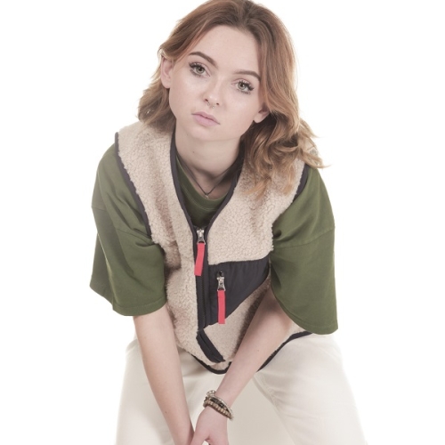 photo of a person leaning forward whilst sat on a block wearing a green shirt and fleece with no arms