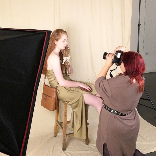 photographer taking an image of a person in a greenish dress sitting on a stool