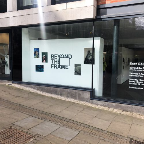 Photo of a gallery from the outside and the wall reads "beyond the frame"