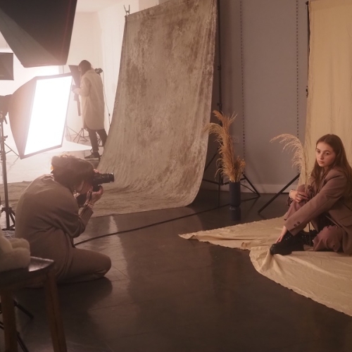 photographer taking an image of a person in a grey jacket and trousers sat on the floor