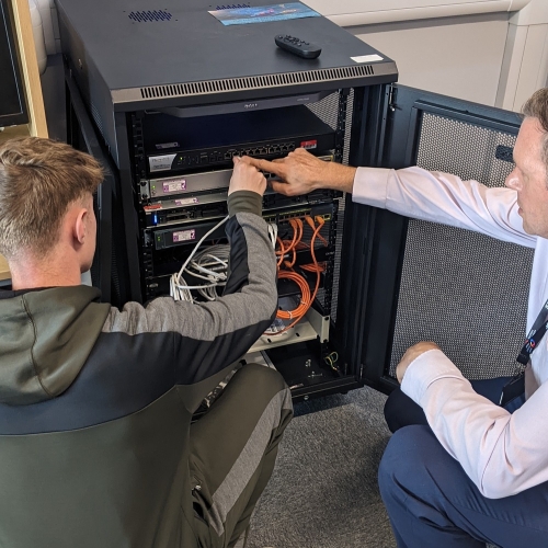 Photo of two people inspecting and plugging wires into a server switch