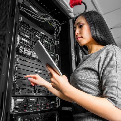 Photo of a person standing next to a server rack looking at a tablet